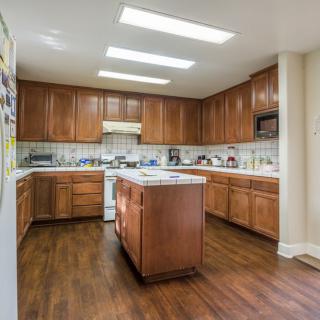 A spacious kitchen with wooden cabinets and flooring, featuring a central island and ample overhead lighting.
