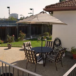 A cozy patio area with a table, chairs, and an umbrella in a garden setting.