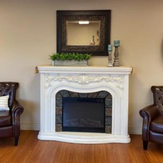 A cozy living room setup featuring a decorative white fireplace flanked by leather armchairs, with a mirror and candles on the mantelpiece.