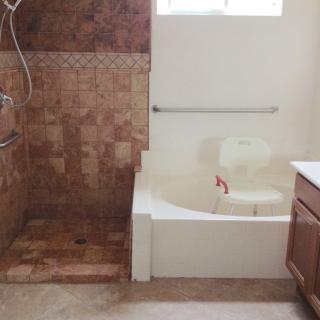 A bathroom featuring a tiled shower area and a bathtub with a grab bar and bath chair.