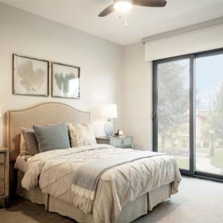 A modern bedroom with a cozy bed and soft lighting, featuring large windows and neutral color tones.