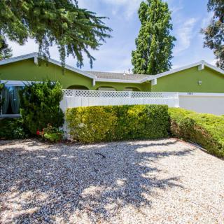 A charming single-story house with a green exterior and well-maintained front yard landscaping.