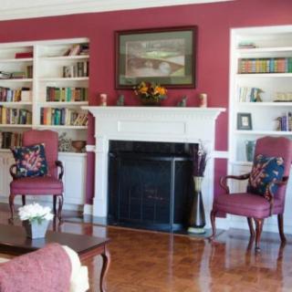 A cozy living room featuring a fireplace surrounded by built-in bookshelves, two upholstered armchairs, and a wooden floor.