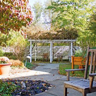 A serene garden setting with a pergola, chairs, and lush greenery.