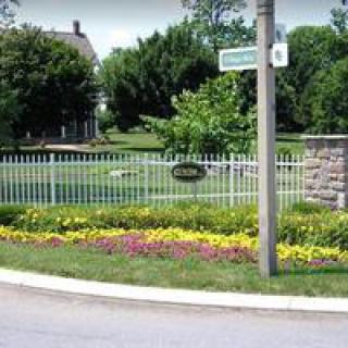 A landscaped garden area with a white fence and colorful flowers on a street corner.