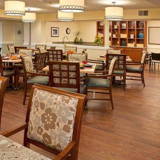 A cozy dining area with neatly arranged tables and chairs, featuring warm lighting and wooden flooring.