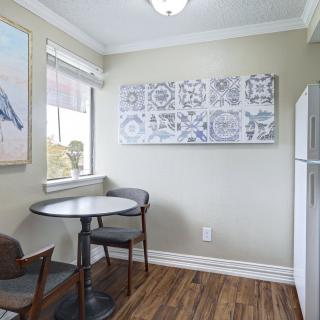 A small kitchen dining area with a round table, two chairs, artwork on the walls, and a refrigerator in the corner.