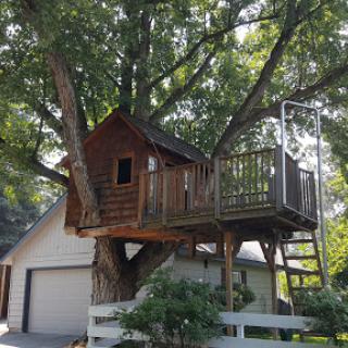 A charming wooden treehouse nestled in a large tree, complete with a deck and ladder, perfect for imaginative play.