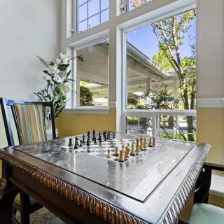 A chessboard set up in a sunny room with large windows and comfortable seating.