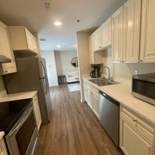 A modern kitchen with white cabinets and wooden flooring, featuring various appliances and bright lighting.