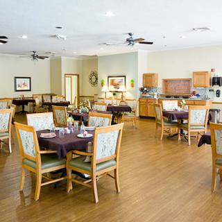 A spacious dining room with multiple tables and chairs, featuring a kitchen area and wood flooring.
