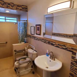 An accessible bathroom with modern amenities, including a sink, mirror, and toilet aid.