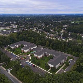 Aerial view of a residential apartment complex surrounded by trees and a suburban neighborhood.
