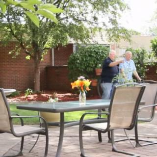 A peaceful garden patio with a table, chairs, and two people enjoying the outdoor setting.