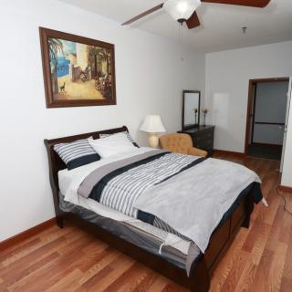 A cozy bedroom with a neatly made bed, a painting on the wall, and wooden flooring.
