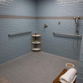 An accessible bathroom with blue tiled walls, featuring a shower area equipped with grab bars and shelves.