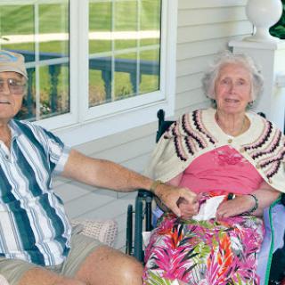 An elderly couple enjoying a sunny day on their porch, sharing a moment of affection.