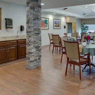 A cozy dining area with tables and chairs, featuring a kitchenette and stone pillar.