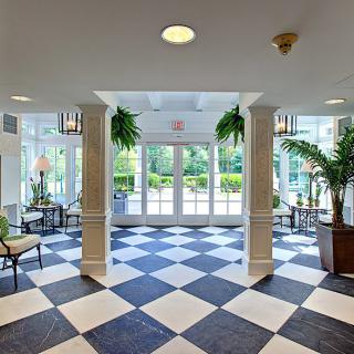 A well-lit lobby featuring black and white checkered floor tiles, lush plants, and comfortable seating areas.