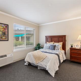 A cozy bedroom with a neatly made bed, wooden furniture, and natural light streaming in through the window.
