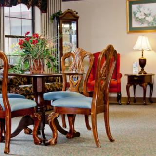 A traditional living room setup featuring a wooden table with chairs, decorative flowers, and a lamp.
