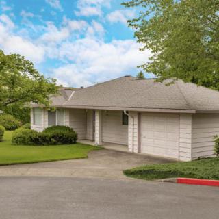 A suburban residential house with a driveway and surrounding greenery under a cloudy sky.