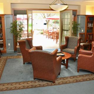 A cozy lobby seating area with armchairs and a table, featuring large windows and plants.