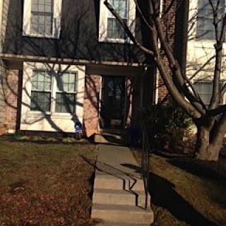 A brick residential house with a front yard and stairs leading to the entrance.