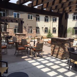 An outdoor patio area with tables and chairs under a wooden pergola, casting shadows on the ground.