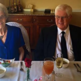 An elderly couple dressed in formal attire enjoying a meal together, possibly celebrating a special occasion.
