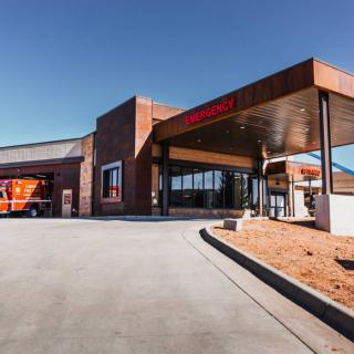 The exterior of a hospital with an emergency entrance and an ambulance parked outside.