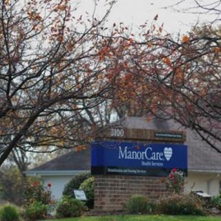 A nursing home sign with a healthcare logo surrounded by autumn trees.