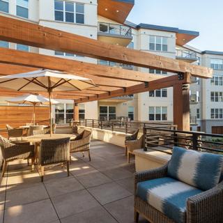 A spacious outdoor patio area with seating, umbrellas, and a view of the surrounding apartment buildings.