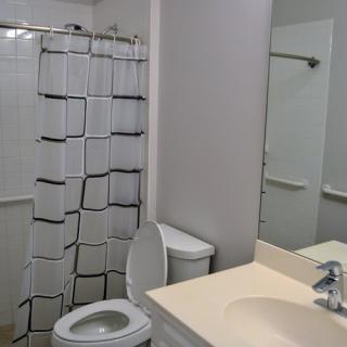 A clean bathroom featuring a shower with a patterned curtain, a toilet, and a sink with a mirror.