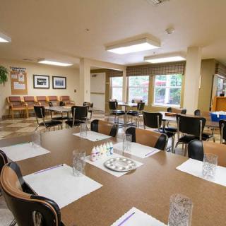 A well-lit dining room with multiple tables and chairs arranged neatly, featuring place settings and large windows.