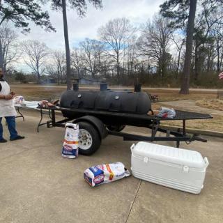 A large barbecue smoker on a trailer set up outdoors with bags of charcoal and a cooler.