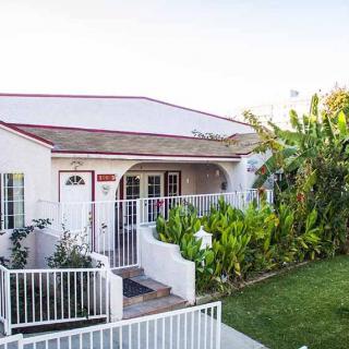 A charming bungalow with a white fence and lush tropical garden.