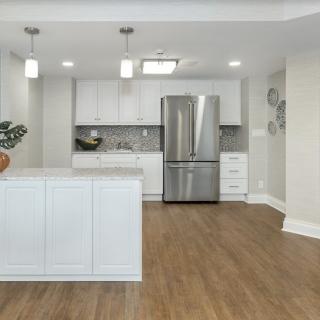 A modern kitchen with white cabinets, stainless steel appliances, and pendant lighting over a hardwood floor.