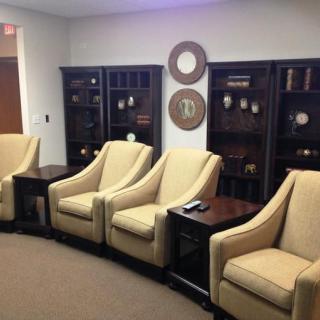 A waiting room with beige chairs and dark wood bookshelves.