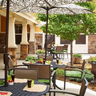 A cozy outdoor patio with tables and umbrellas, surrounded by greenery and stone accents.