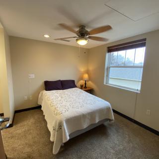A cozy bedroom featuring a bed with white linens, a bedside lamp, and a ceiling fan.