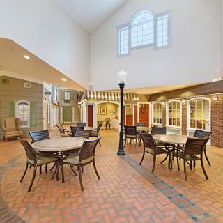 A spacious indoor dining area with round tables and chairs, featuring a brick floor and large windows.