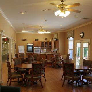 A cozy dining area featuring multiple tables and chairs, with a kitchen setup in the background and ceiling fans overhead.