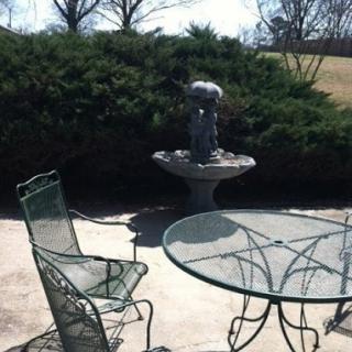 A serene outdoor patio featuring a fountain and metal chairs surrounded by lush greenery.