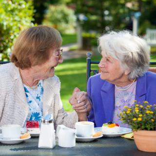 Two elderly women enjoying a conversation and coffee in a garden setting.