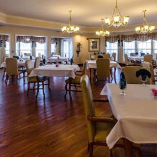 An elegant dining room with neatly arranged tables and chairs, featuring chandeliers and wooden flooring.