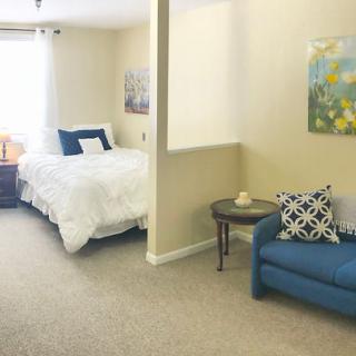 A cozy bedroom with a bed, blue couch, and decorative pillows, featuring wall art and neutral tones.