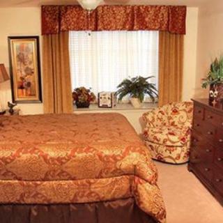 A cozy bedroom with warm decor, featuring a bed, dresser, and window with curtains.