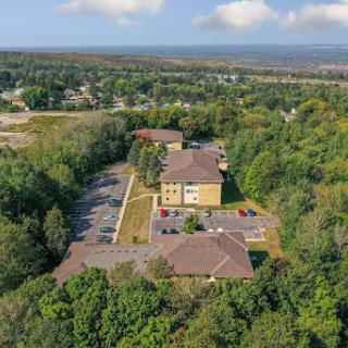 A serene aerial view of a building surrounded by lush greenery and a parking area.