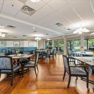 An inviting dining area with neatly arranged tables and chairs, illuminated by soft lighting and complemented by warm wood flooring.